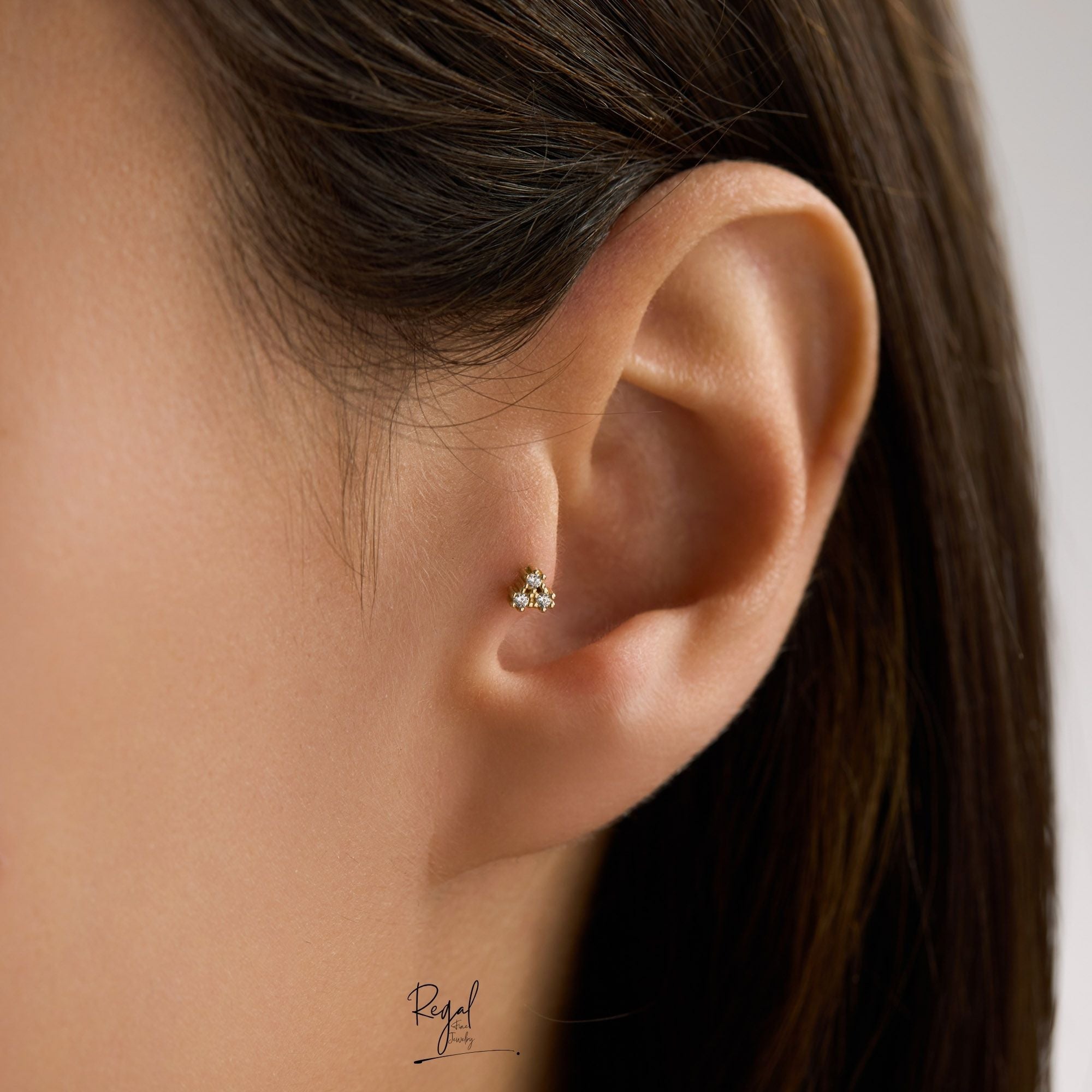 Close-up of an ear wearing a 14K solid gold trinity CZ cluster piercings on the tragus