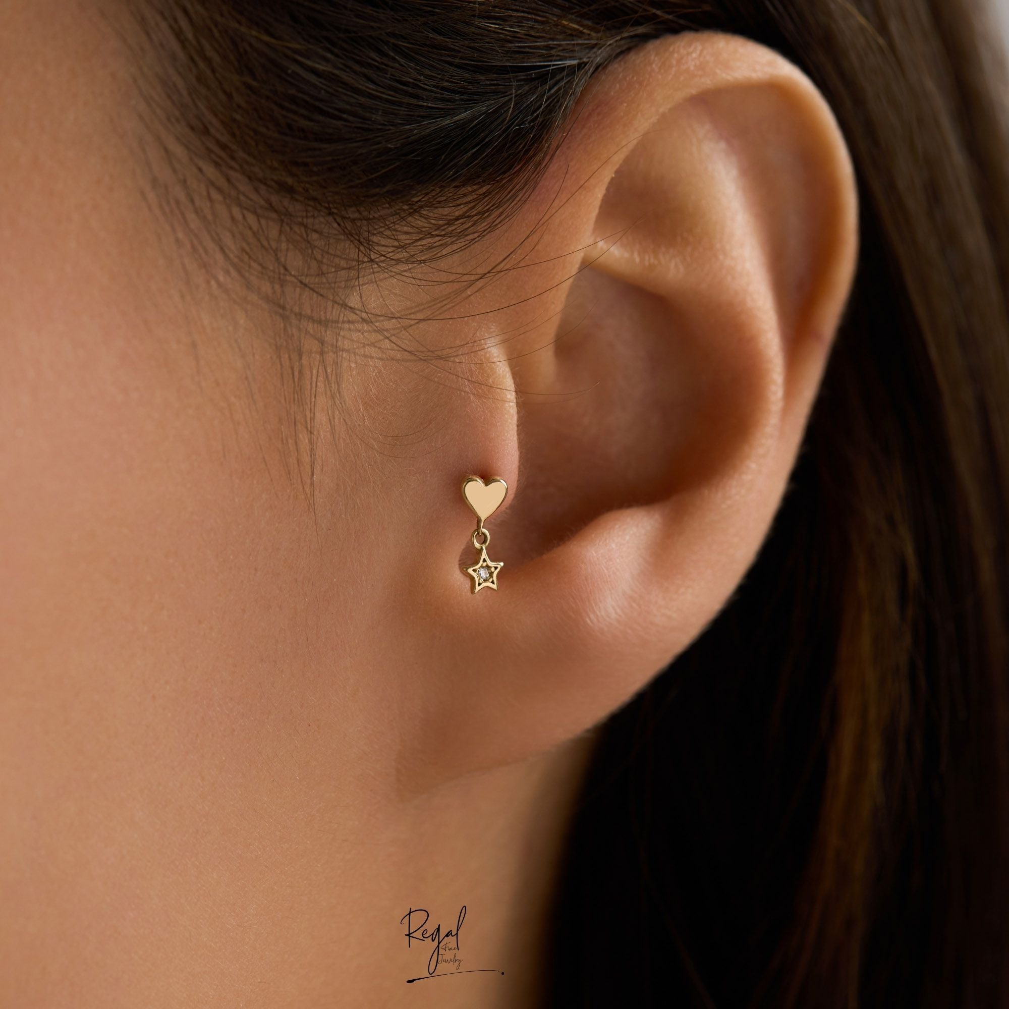 Close-up of an ear wearing a gold heart and star Piercing on tragus.