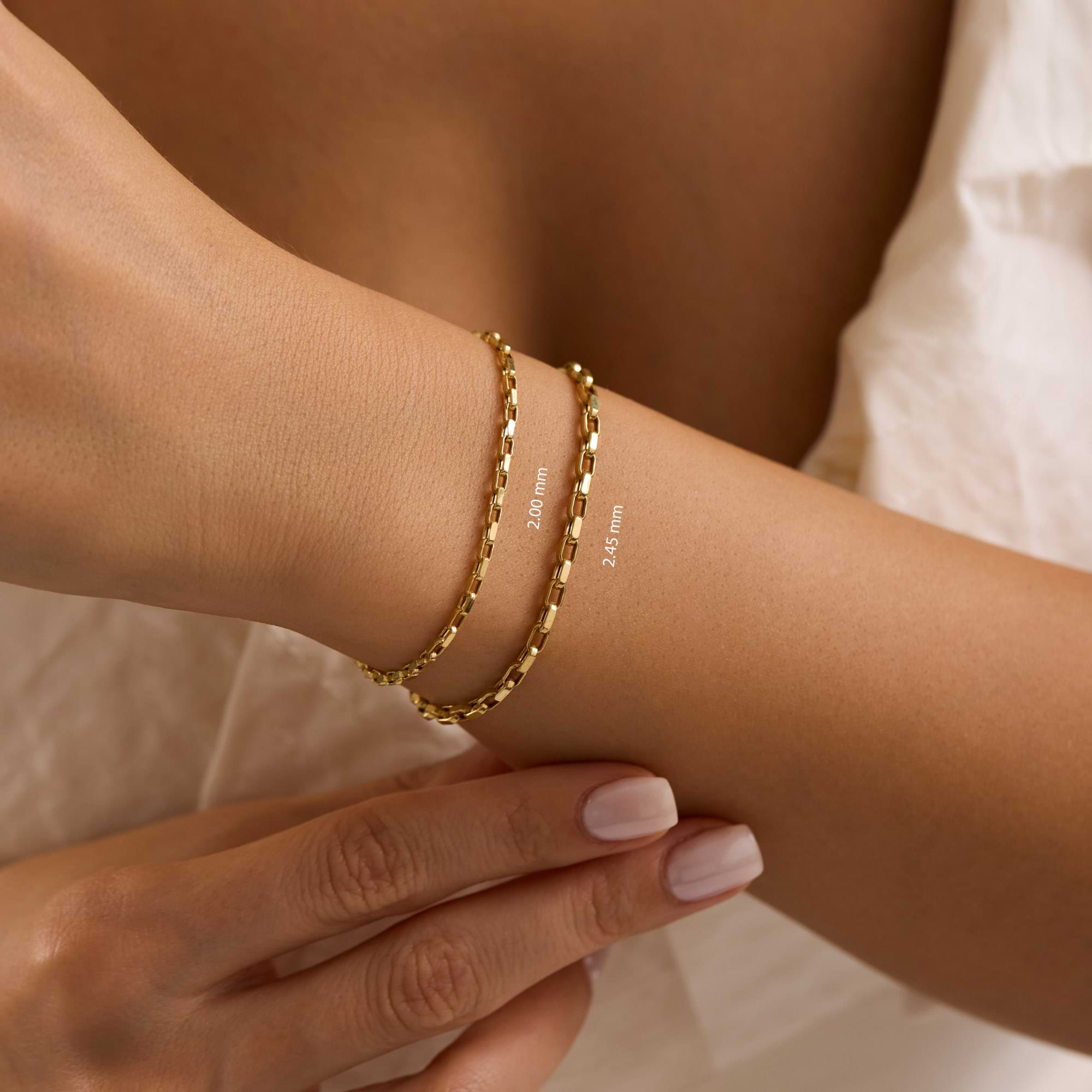 Gold cable chain bracelets on a woman's wrist wearing white dress
