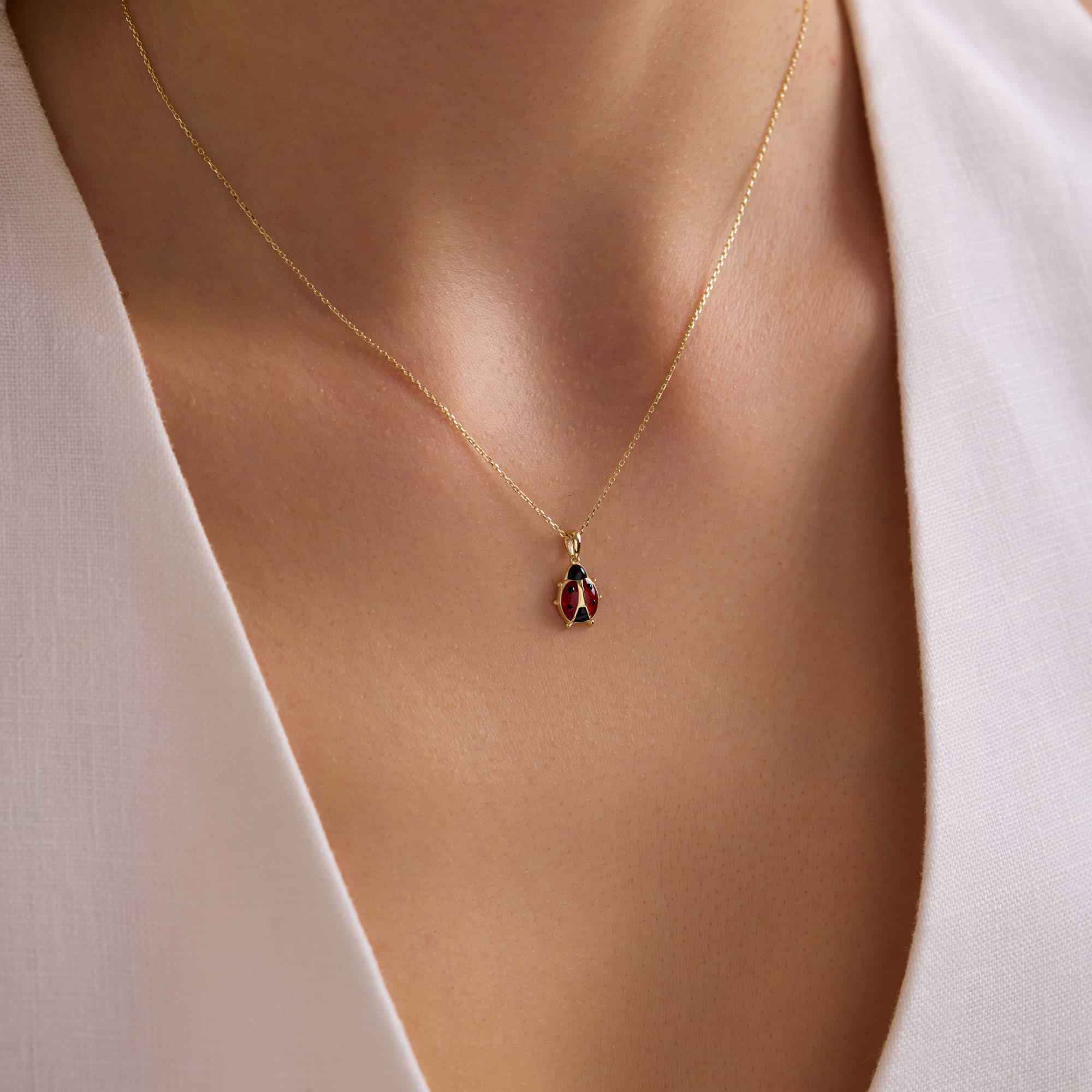 14k Gold necklace with a ladybug pendant on a woman wearing a white top.