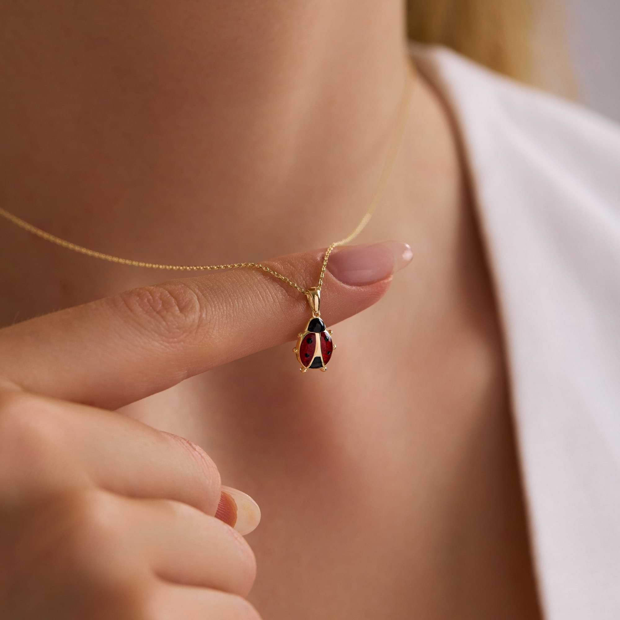 14k Gold necklace with a pendant held by a hand against a neutral background