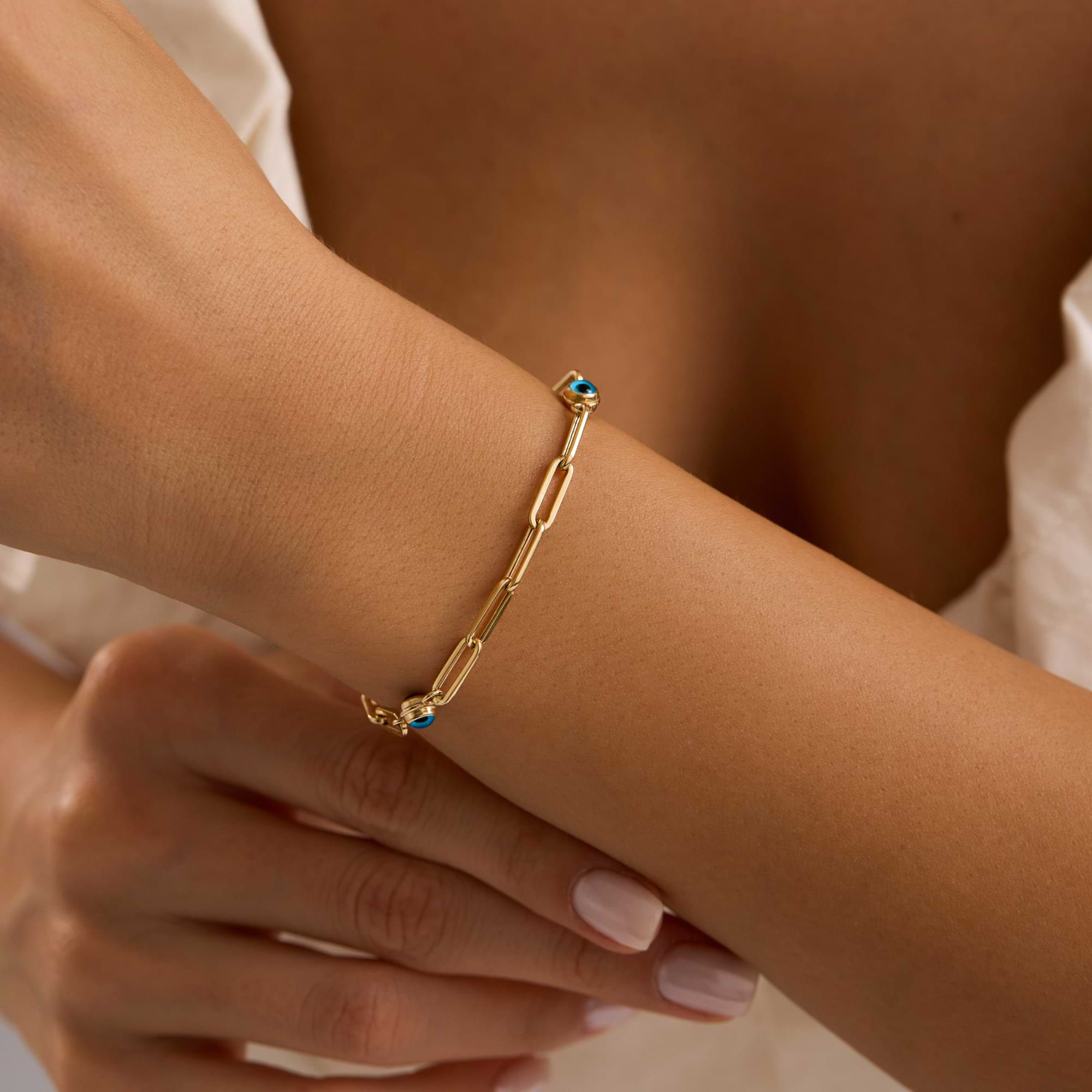 Gold bracelet with blue enamel evil eye on a wrist against a neutral background