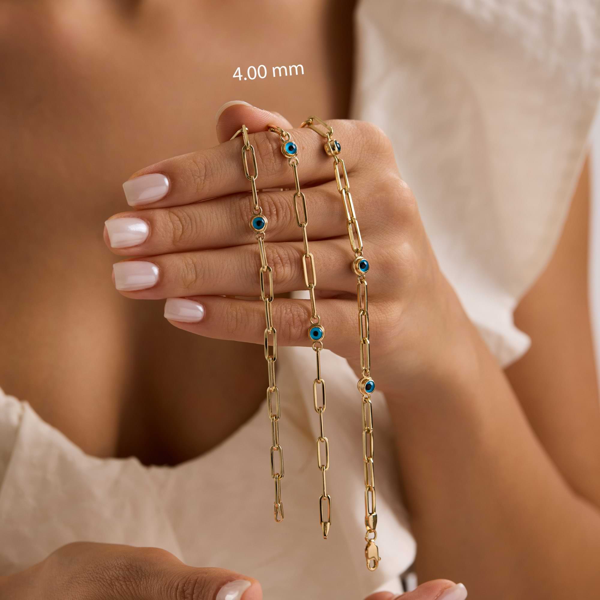Gold bracelet with blue evil eye charms on a wrist against a neutral background