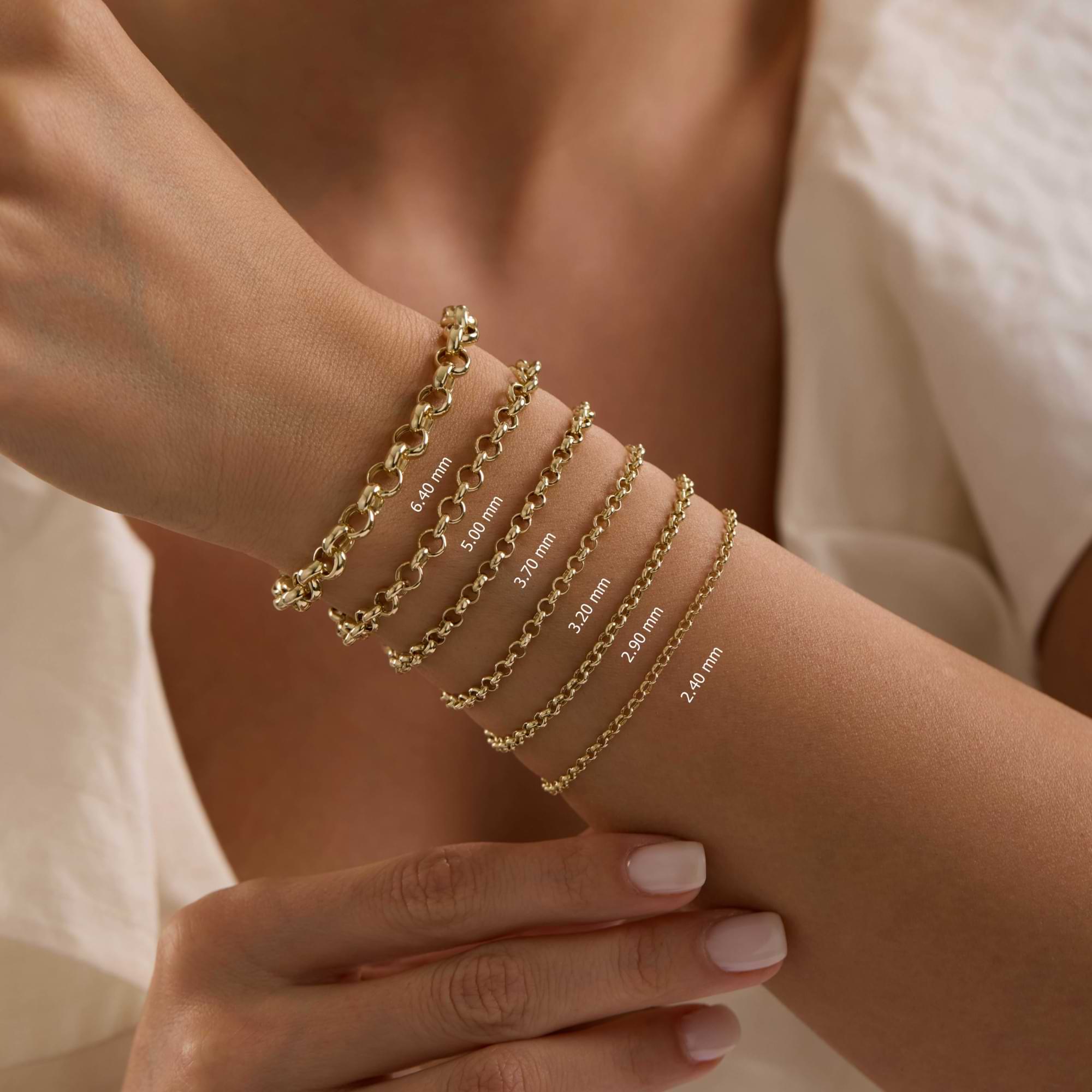 14k Gold rolo chain bracelets of different thicknesses on a wrist with a neutral background