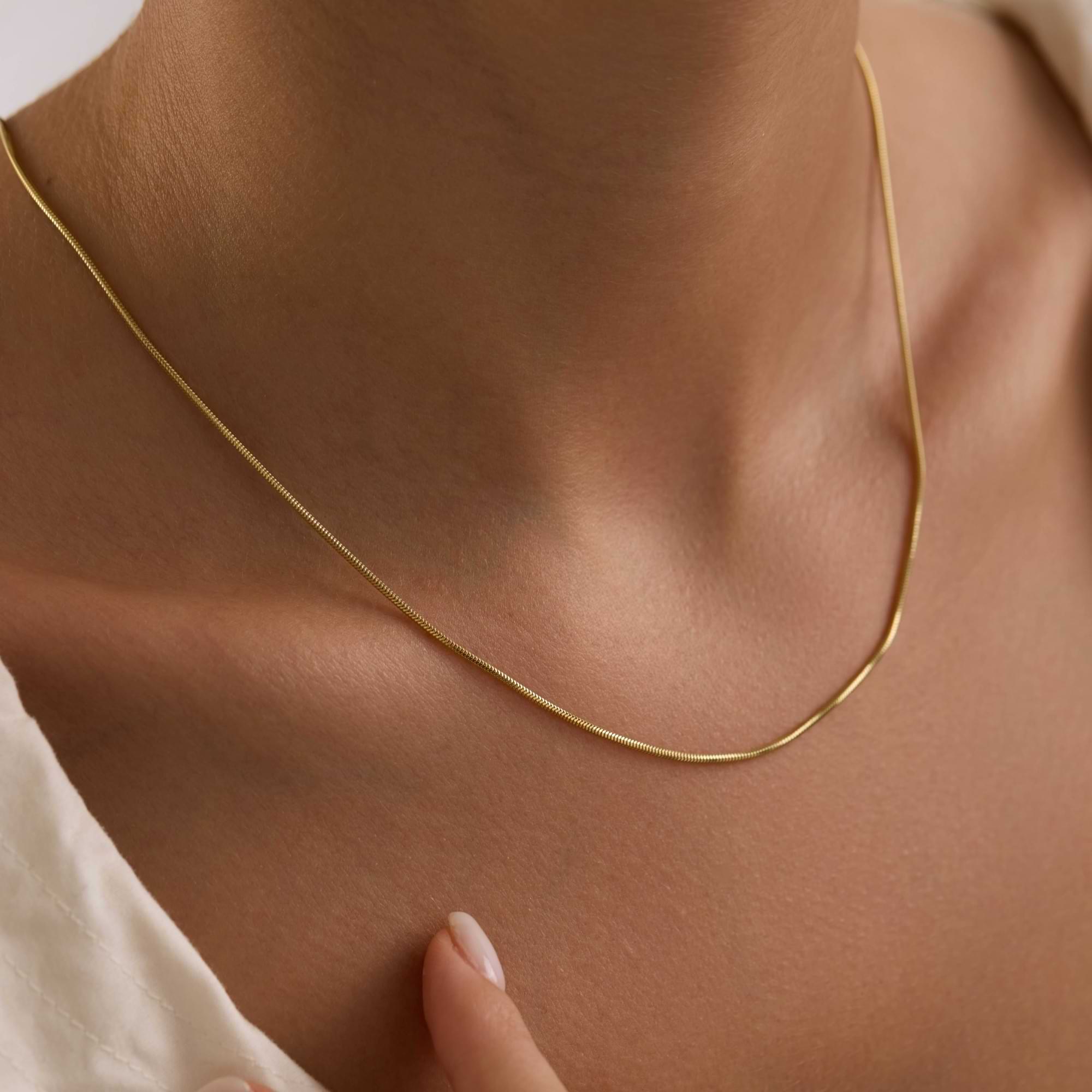 14k solid Gold 1.25mm round snake chain necklace on a person's neck with a neutral background