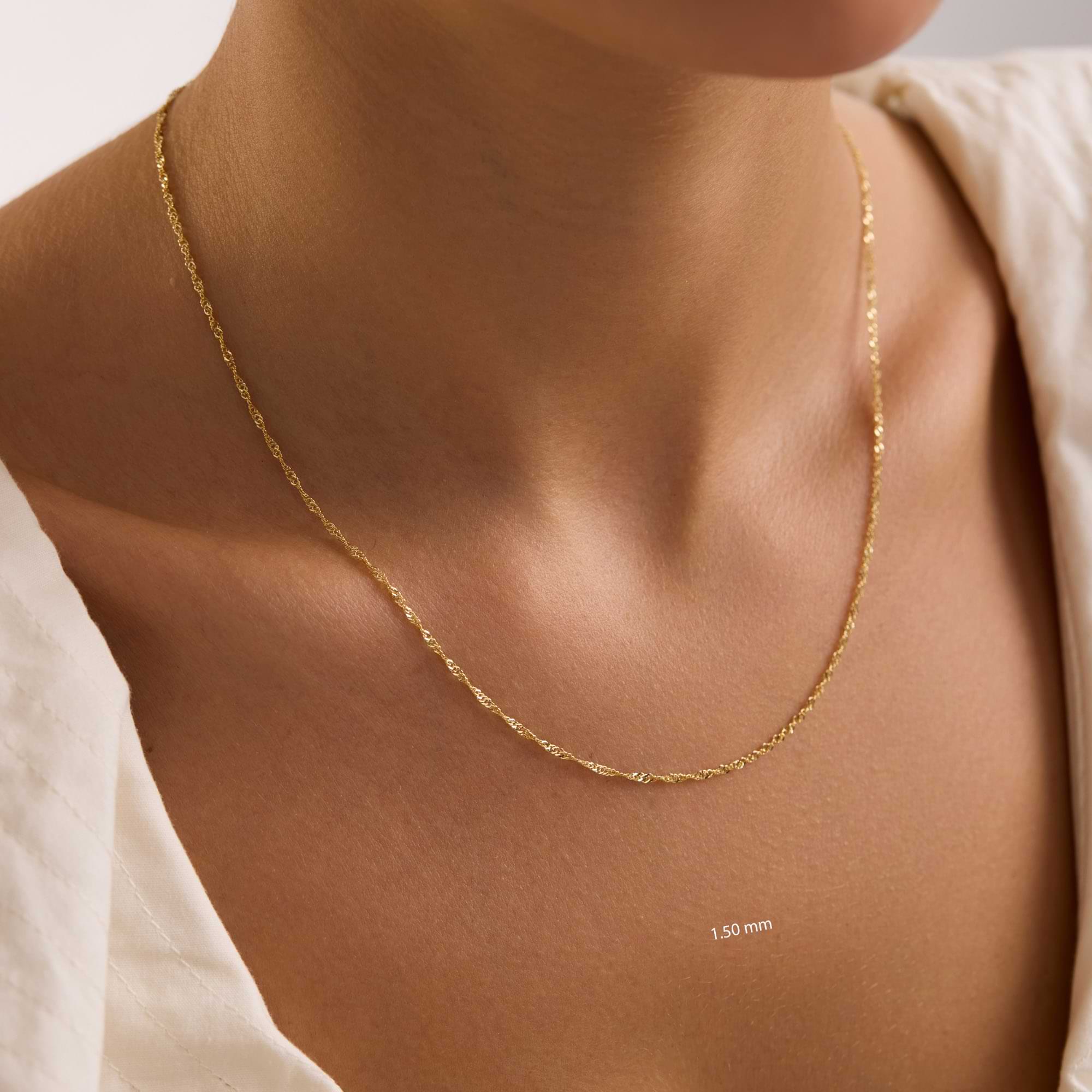 Gold 1.5mm singapore chain on a person's neck with a neutral background