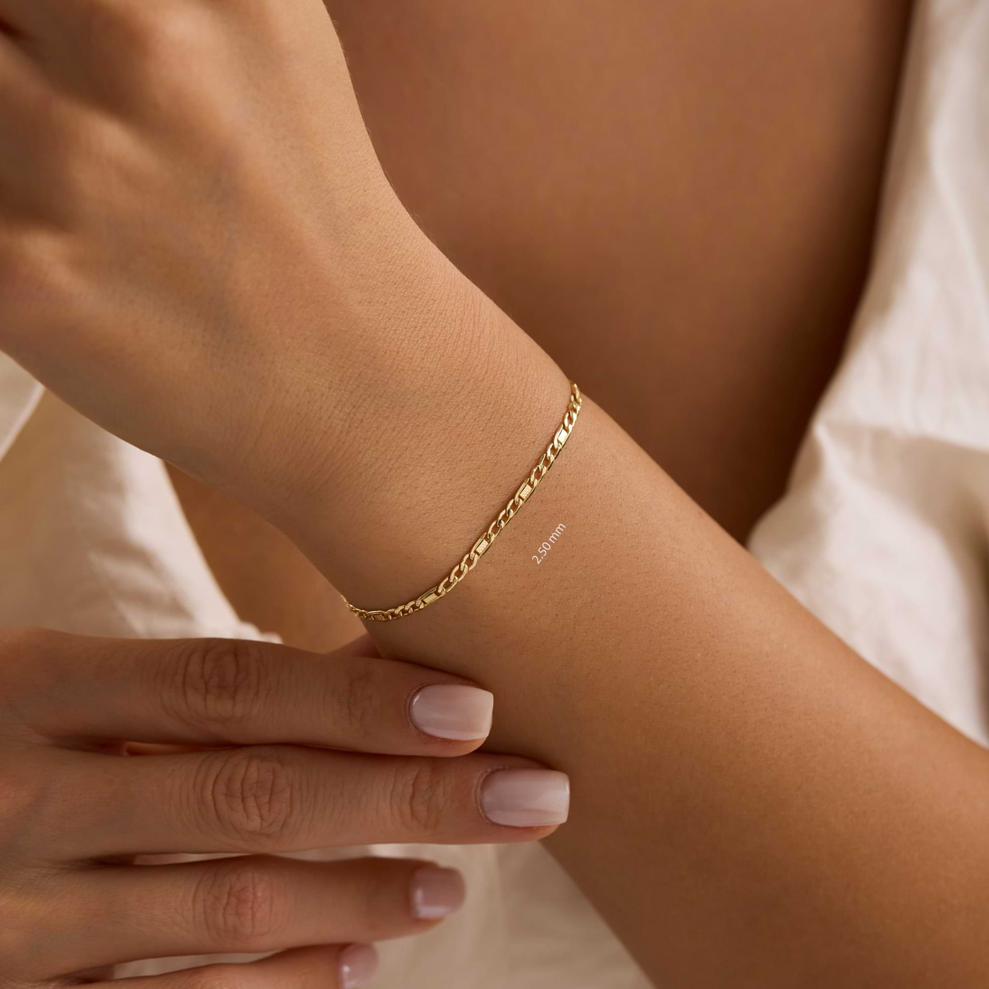 Gold textured figaro 2.5mm bracelet on a wrist of woman wearing white dress.