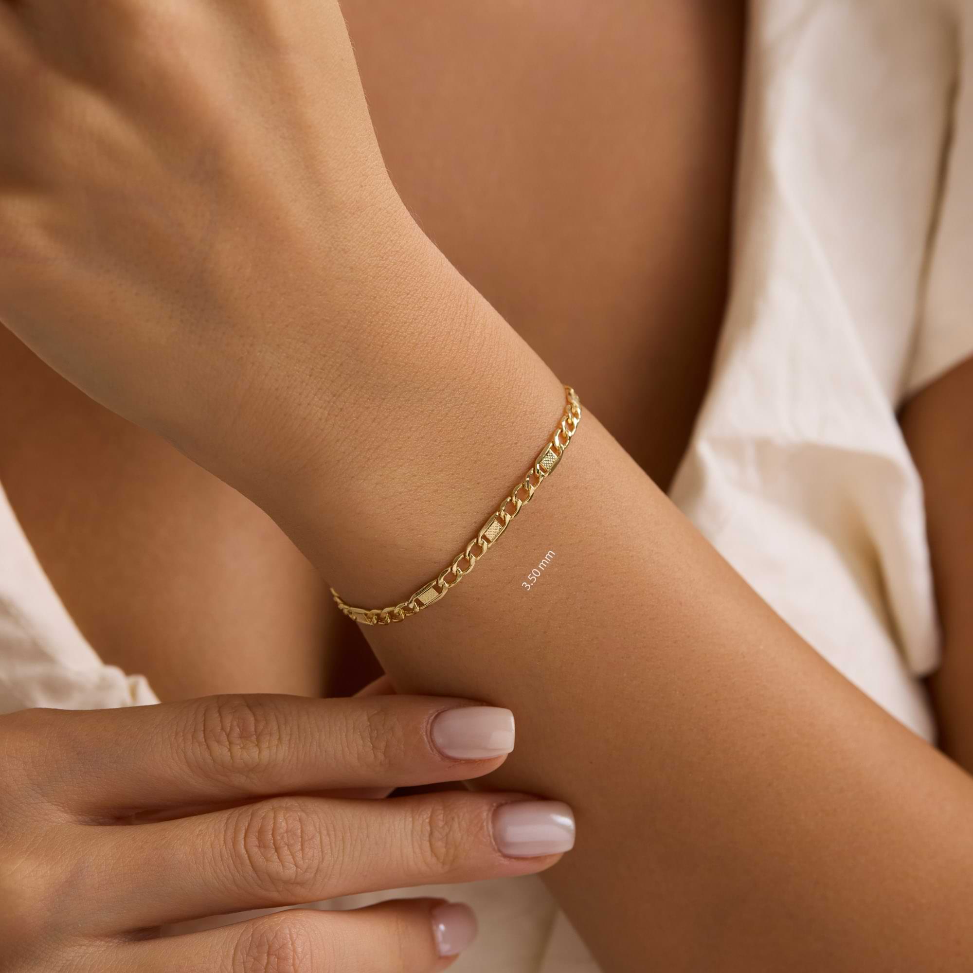 Gold textured figaro 3.5mm bracelet on a wrist of woman wearing white dress.
