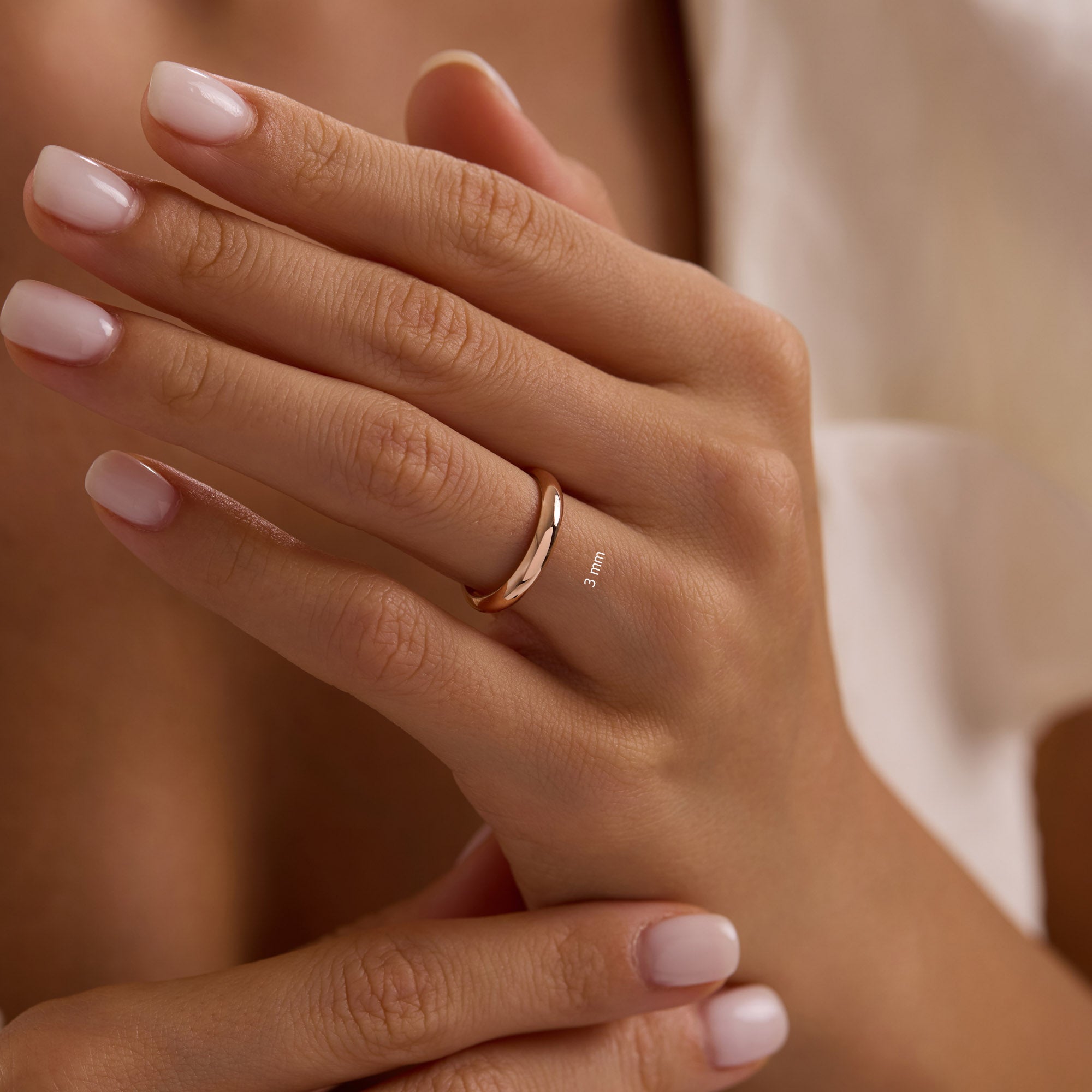 Close-up of hand wearing 3mm 14k rose gold dome wedding band.