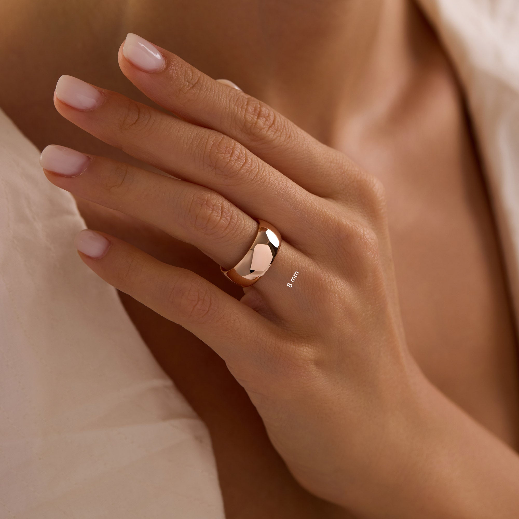 woman's hand with neutral manicure showcasing bold 8mm 14k rose gold wedding band