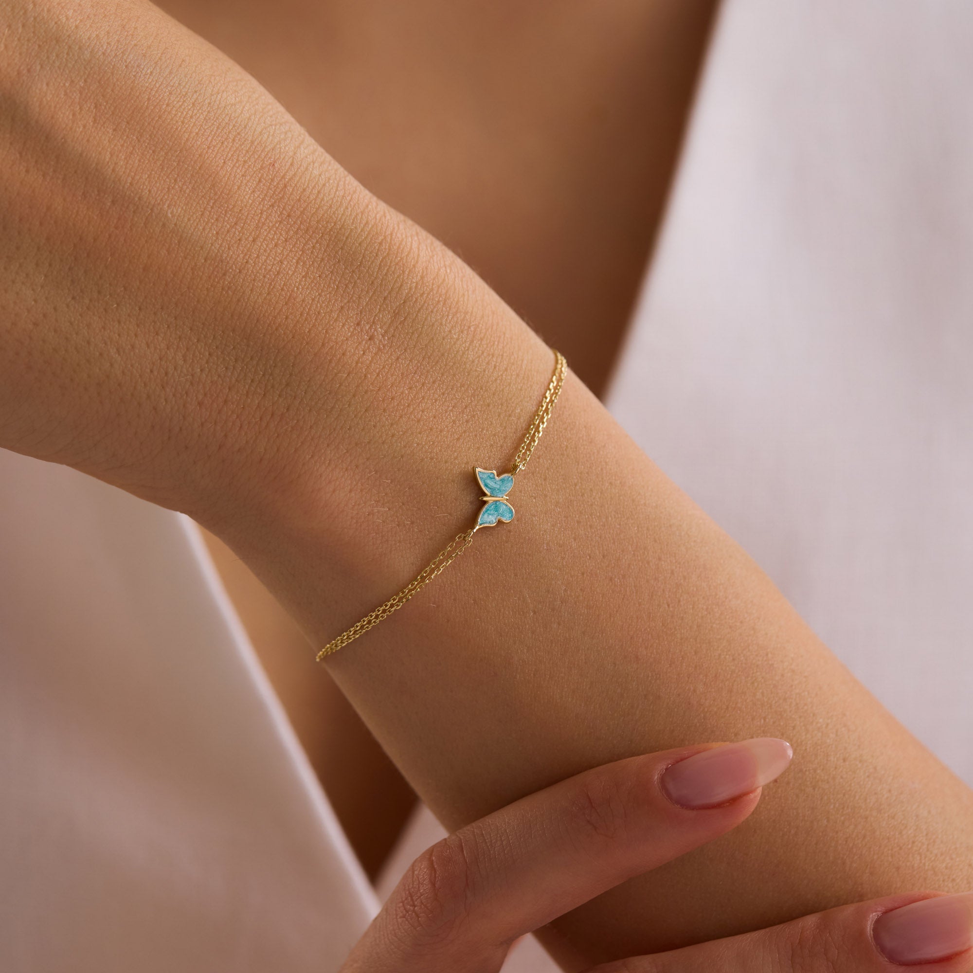 14k Gold double chain bracelet with blue enamel butterfly charm worn on woman's wrist