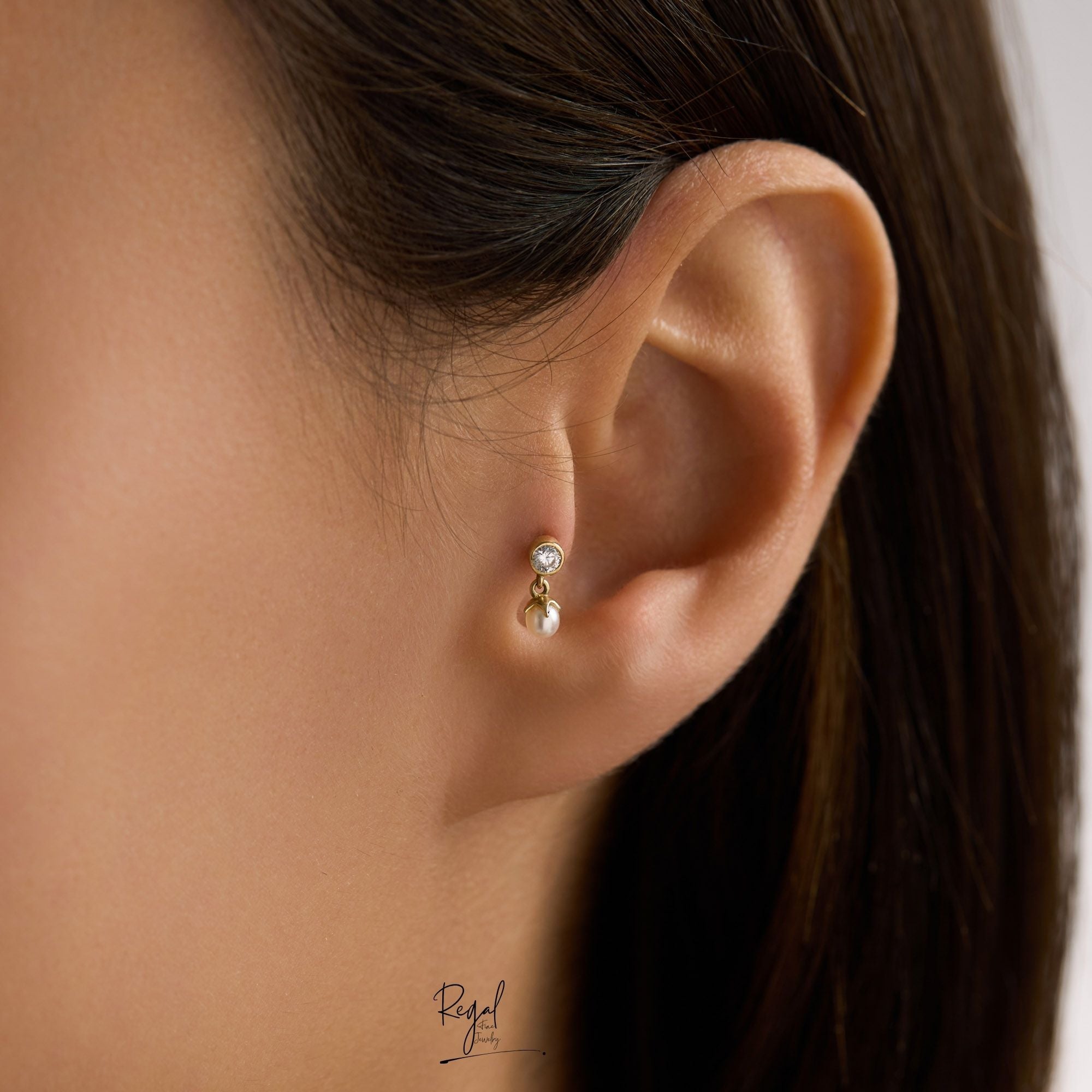 Close-up of an ear wearing a gold dangle piercing on tragus with pearl and cz stones.