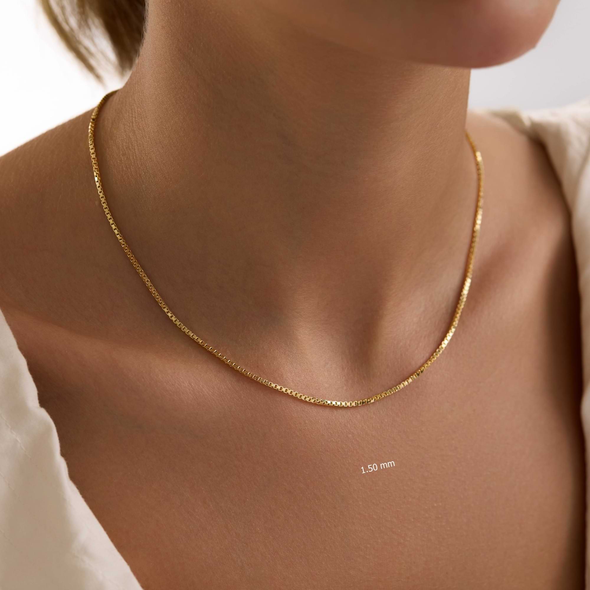 Gold 1.5mm box chain necklace on a person's neck with a close-up view