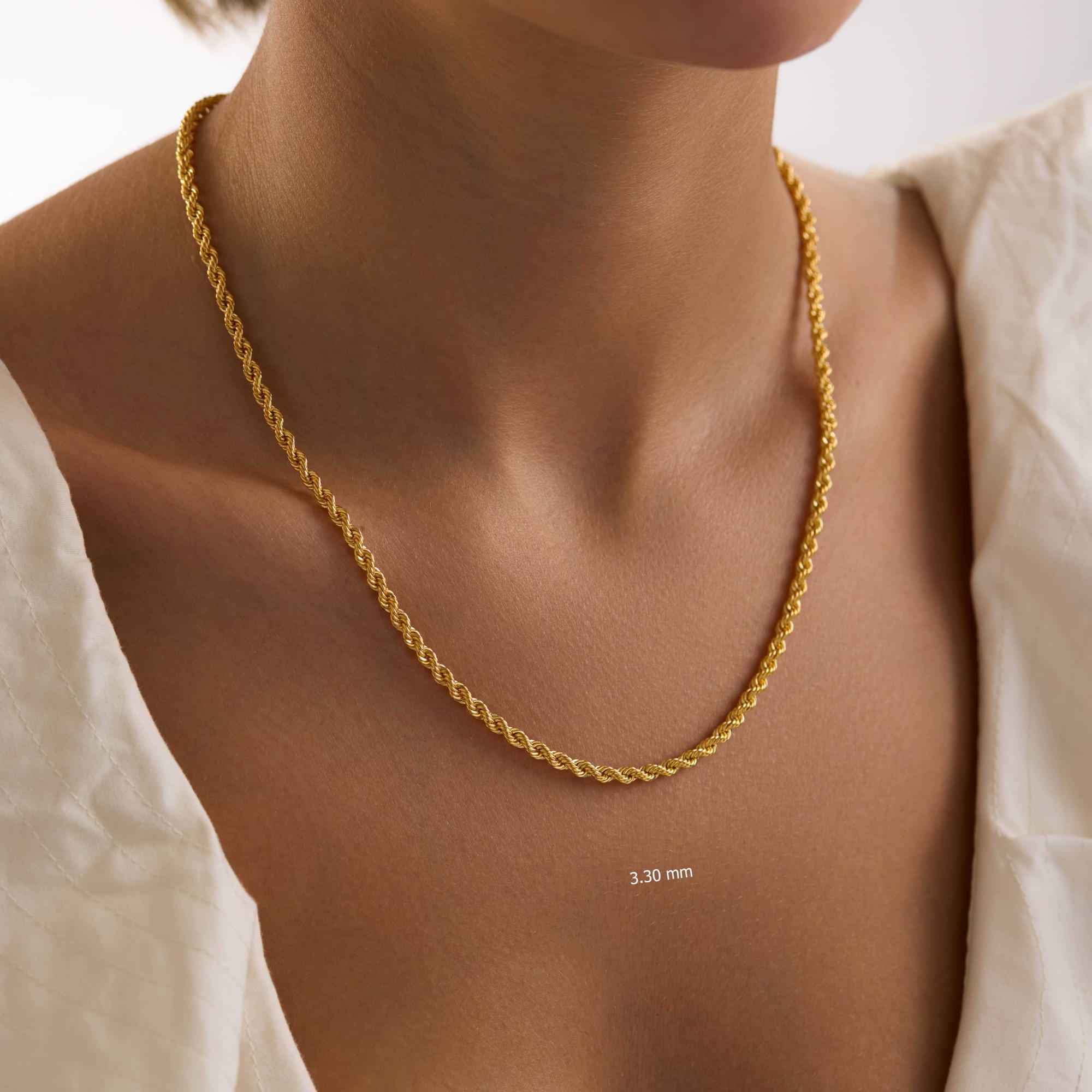 Gold rope chain necklace on a woman wearing white clothing on a plain background