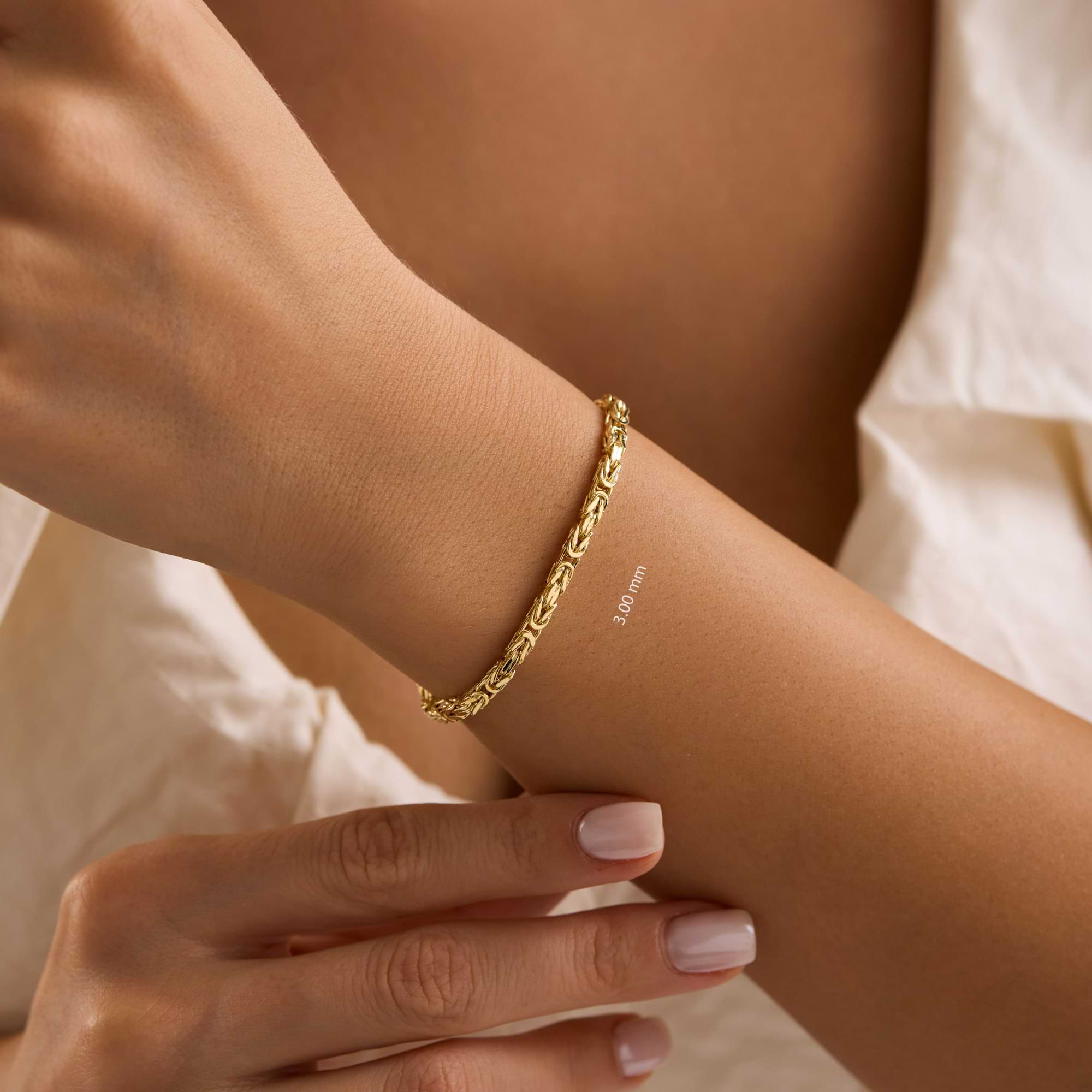 Gold 3mm byzantine chain bracelet on a wrist of woman wearing white dress