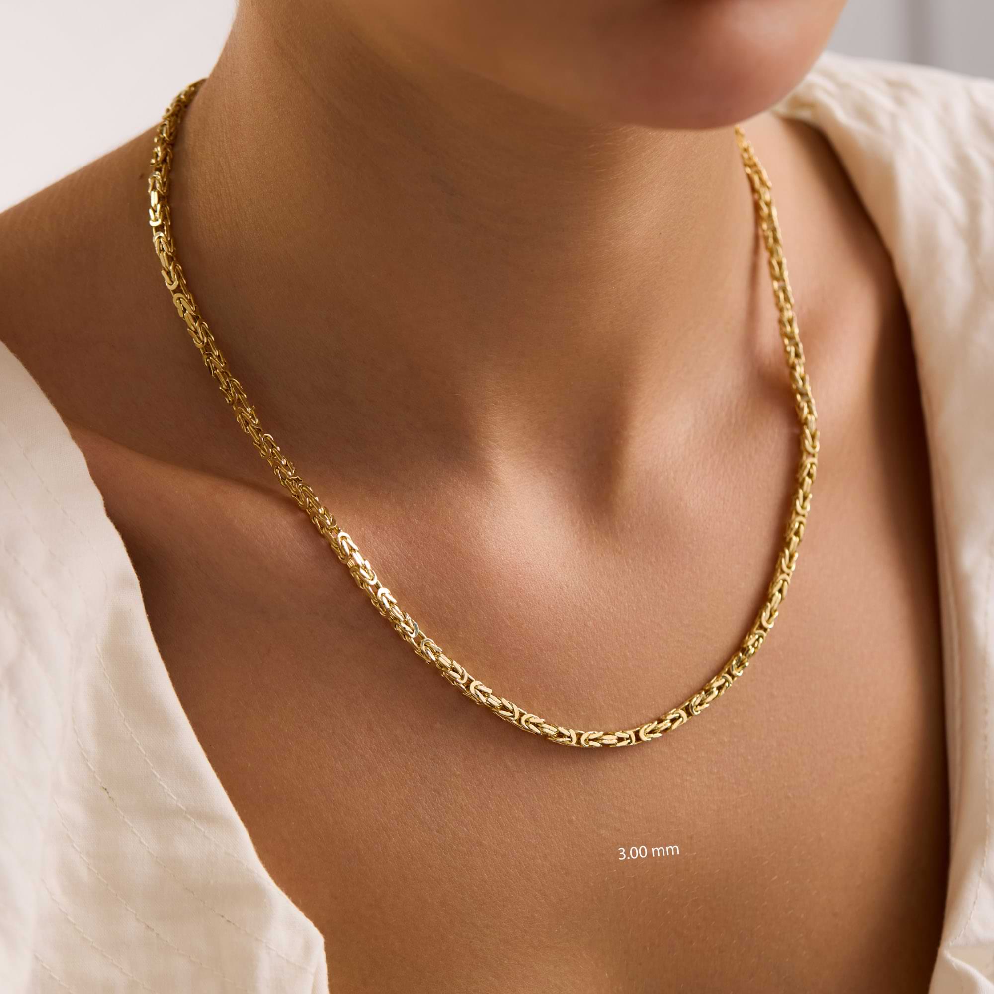 Gold 3mm byzantine chain necklace on a person's neck with a plain background