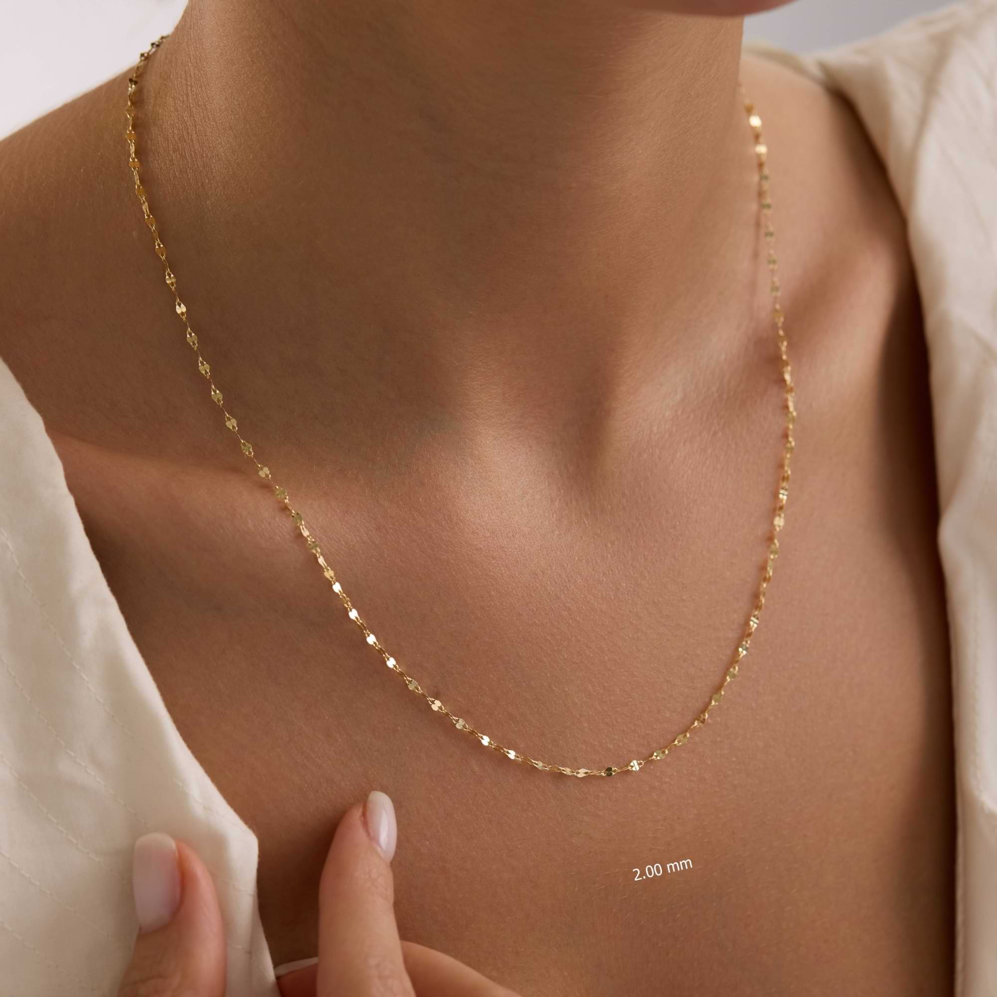Gold 2mm sequin necklace on a person's neck with a neutral background