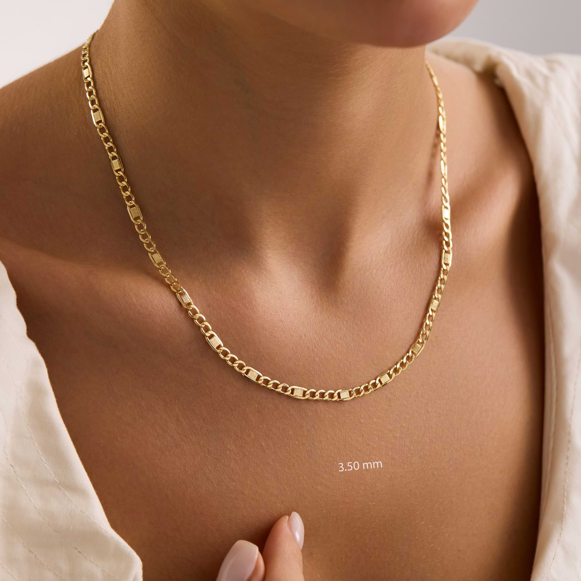 Gold 3.5mm textured figaro chain necklace on a person's neck with a neutral background