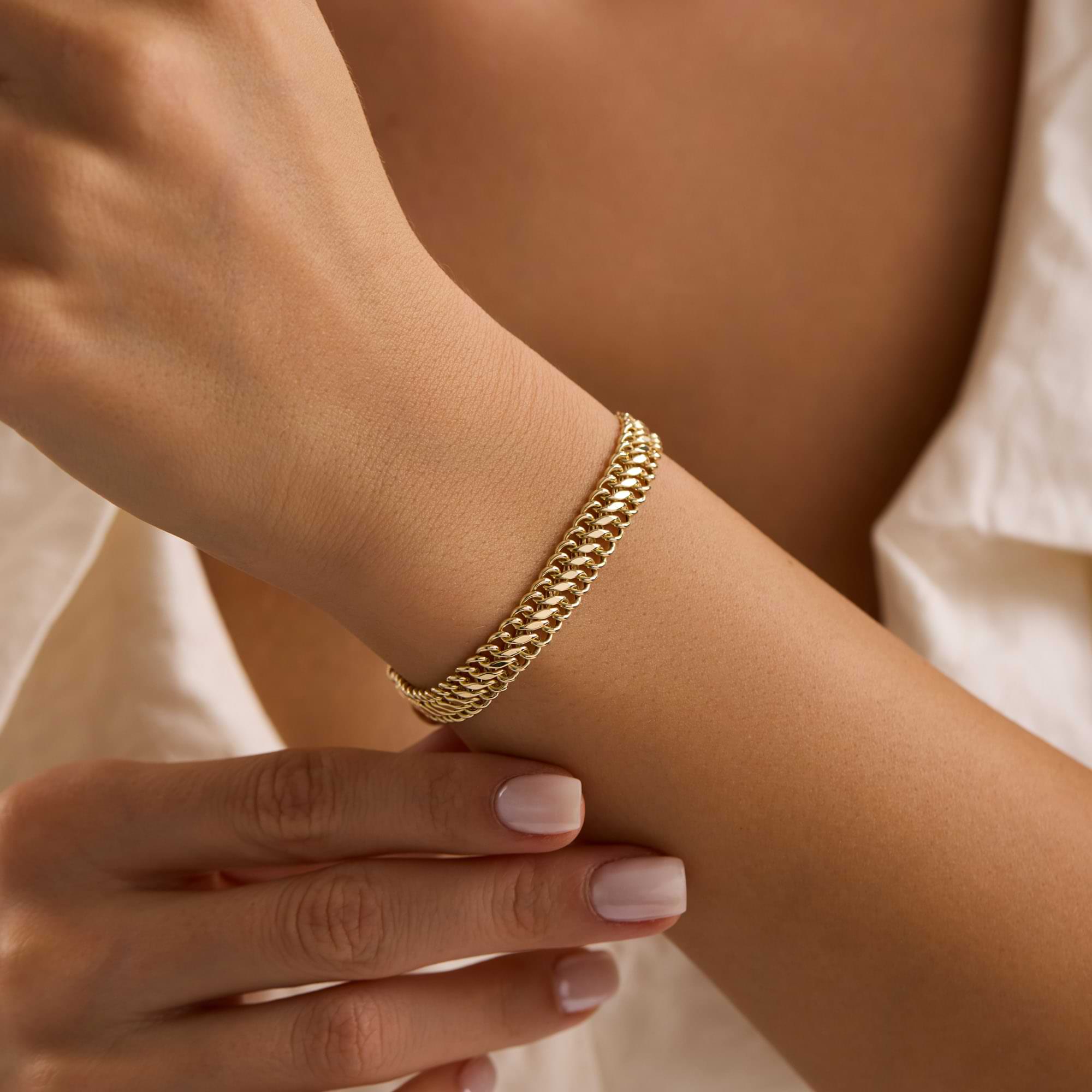 Gold vienna 7.7mm chain bracelet on a wrist of woman wearing white dress