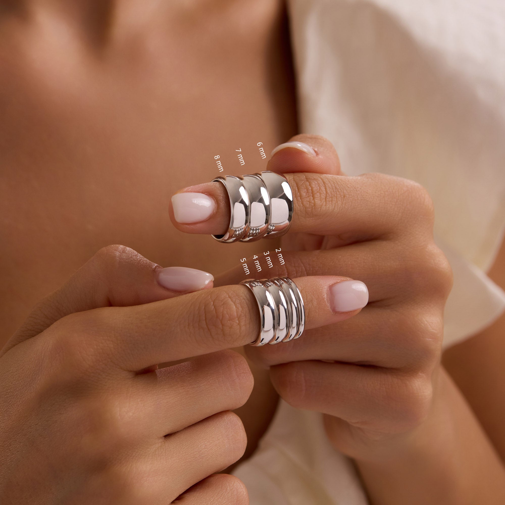 Model holding stacked 14k solid white gold wedding bands on thumbs, showing band widths from 2mm to 8mm.