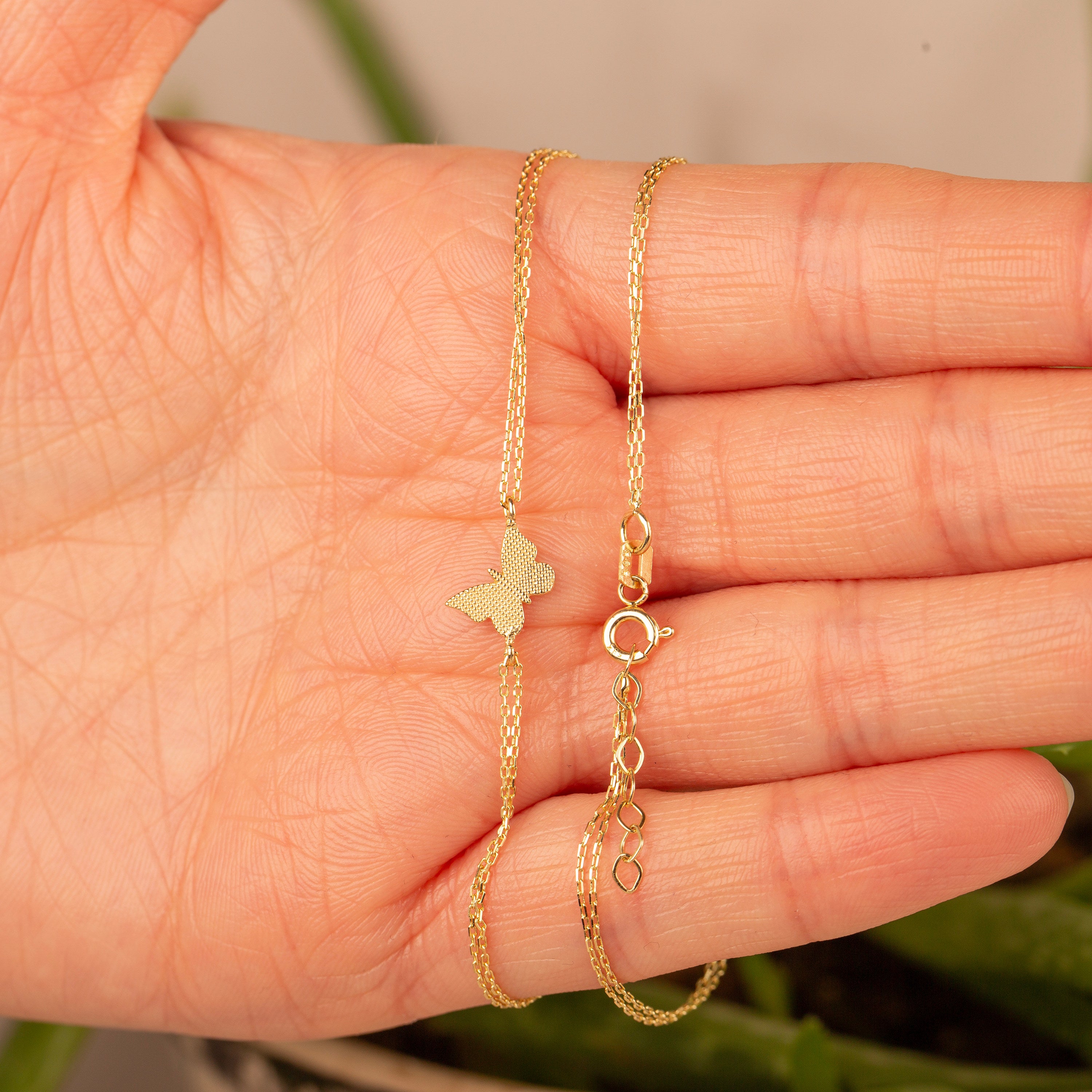 14k gold double chain butterfly bracelet with spring ring clasp and adjustable extender chain held in hand