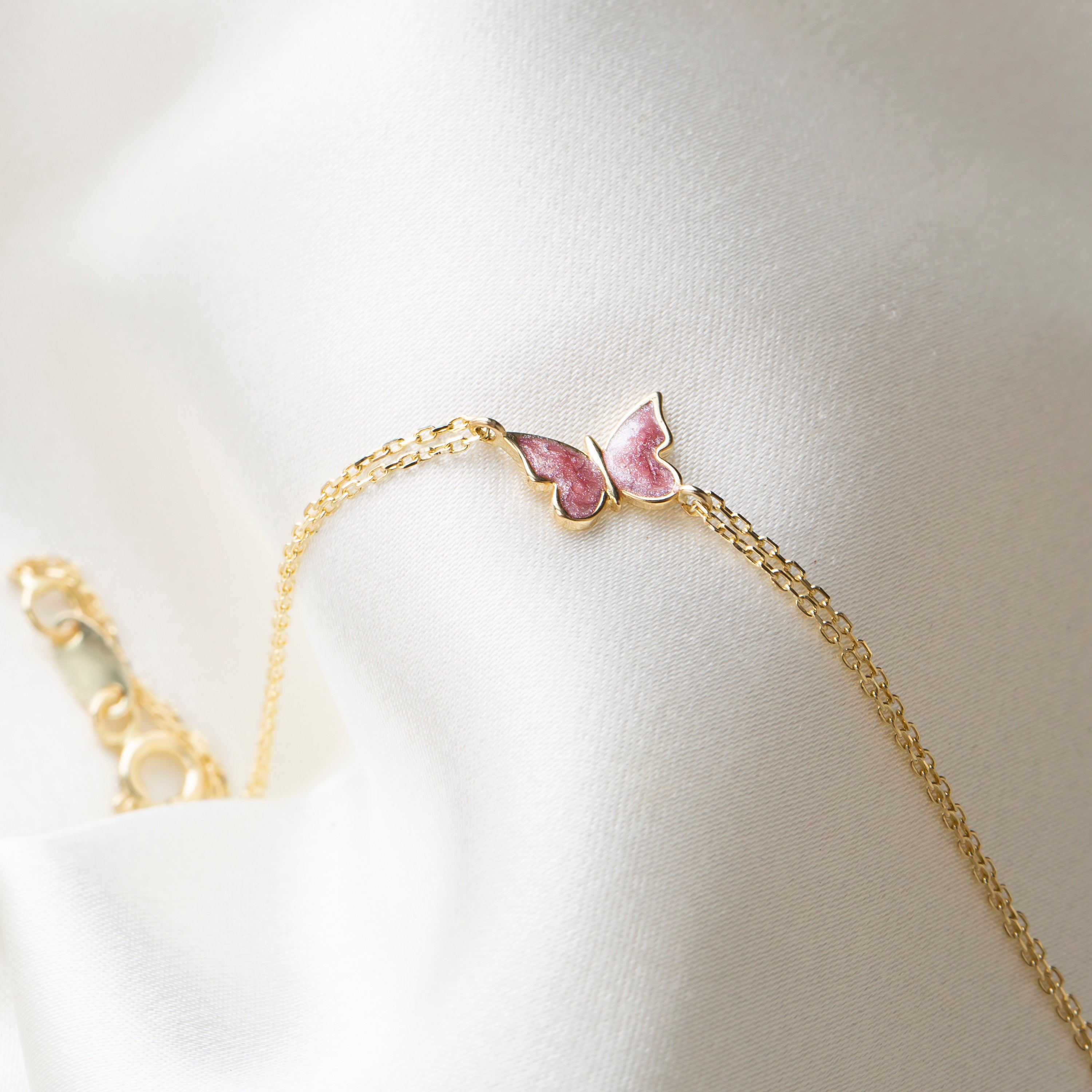 Gold bracelet with a pink butterfly charm on a light background