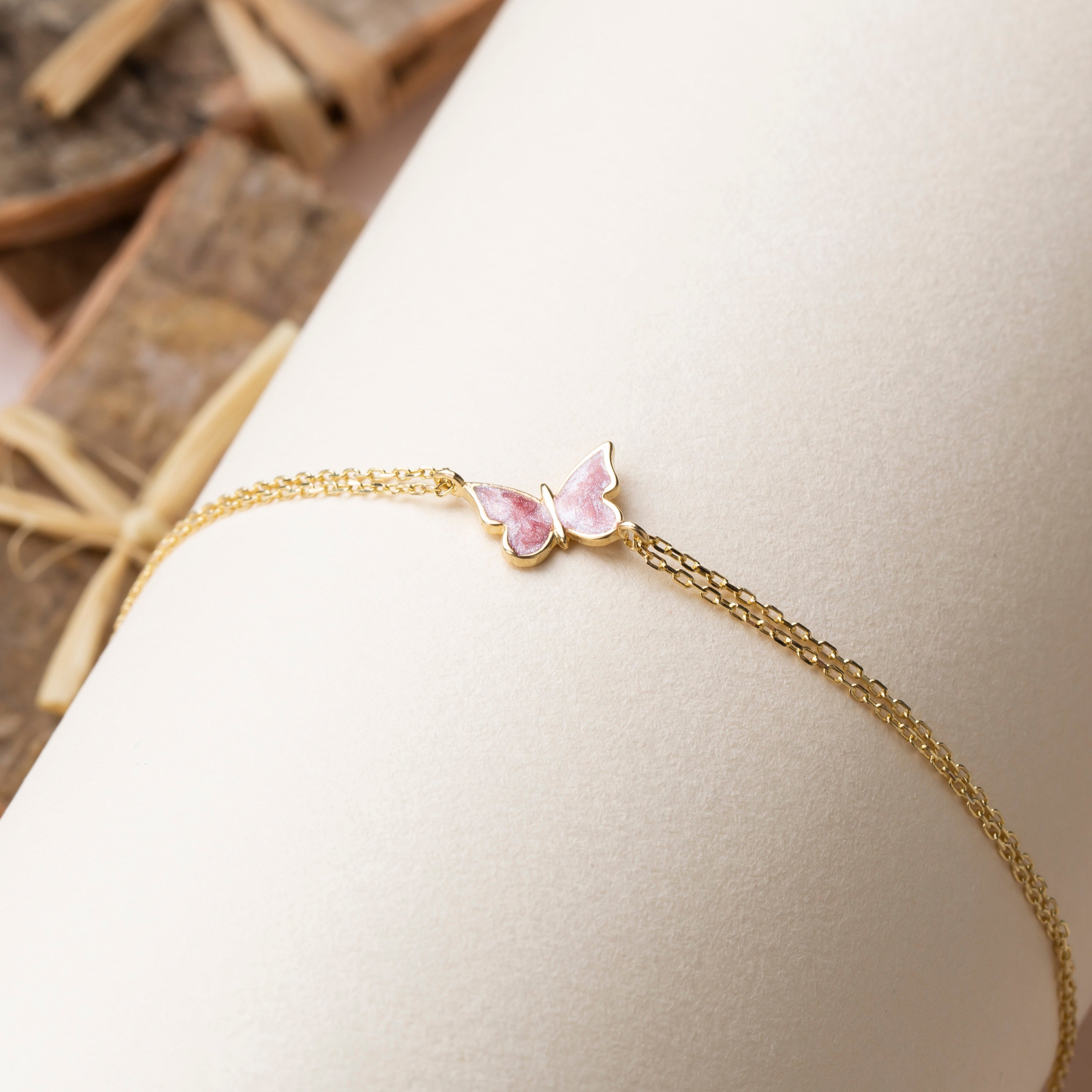 Gold bracelet with a pink butterfly charm on a white surface