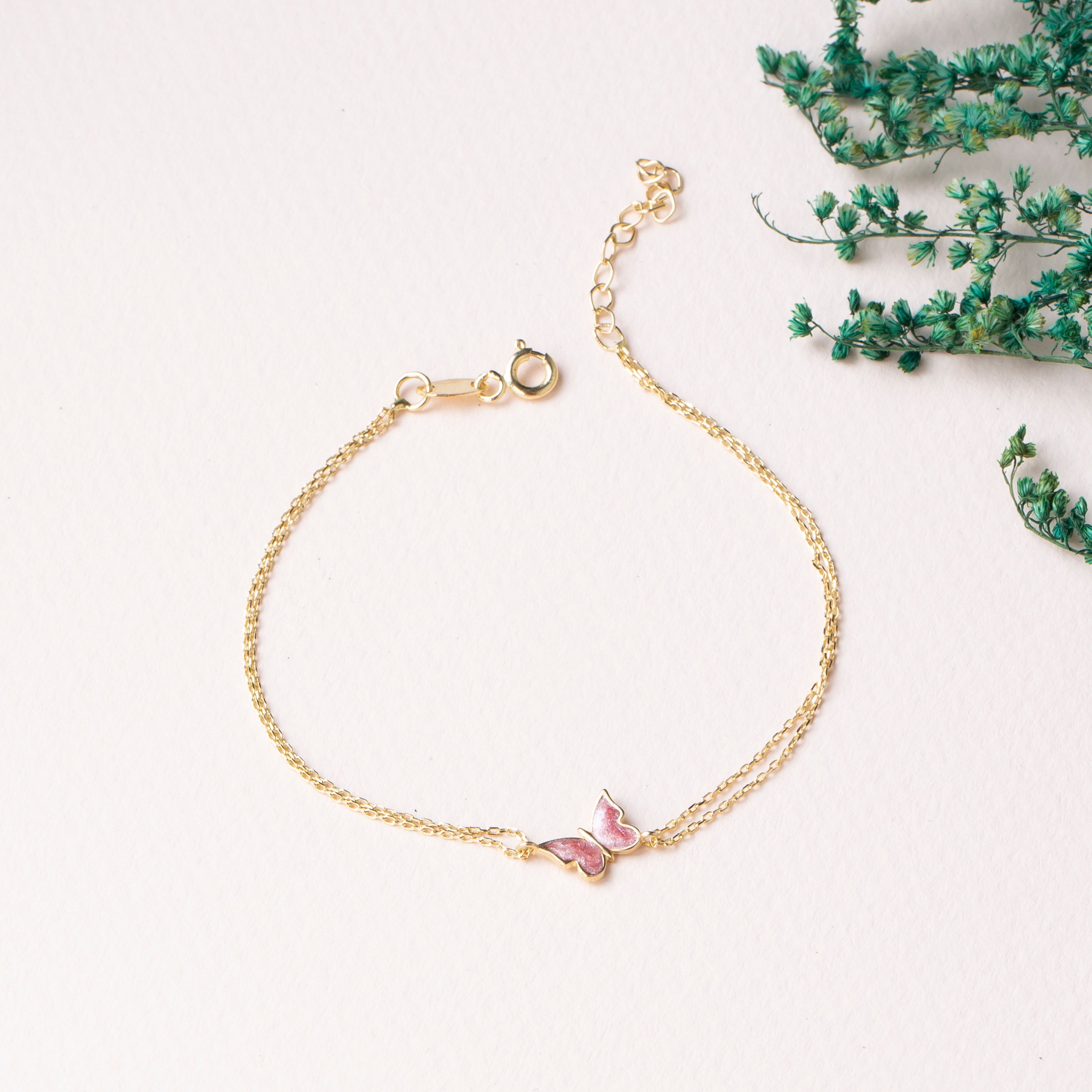 14k Gold bracelet with a pink butterfly charm on a white background