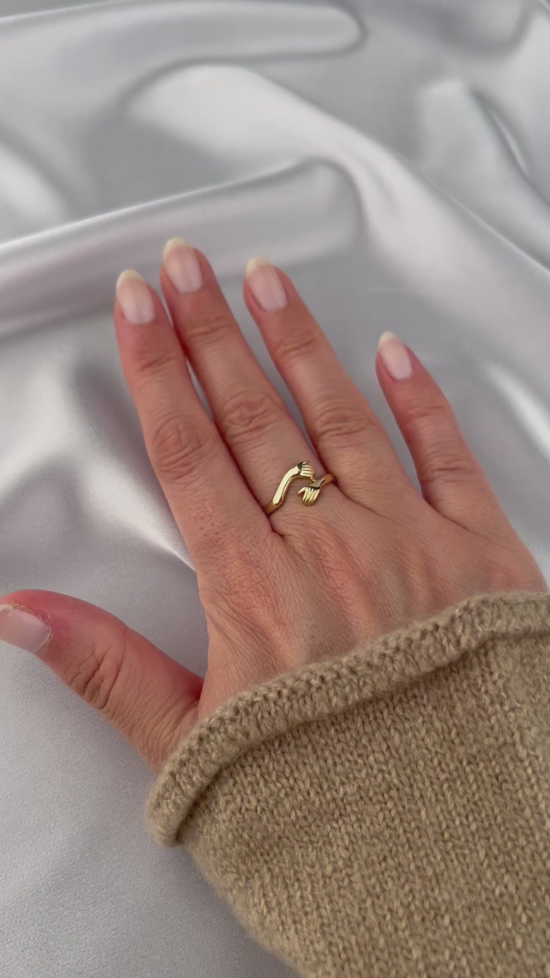 woman with painted nails wearing 14k gold hug ring with long beige sweater on white background show casing the ring