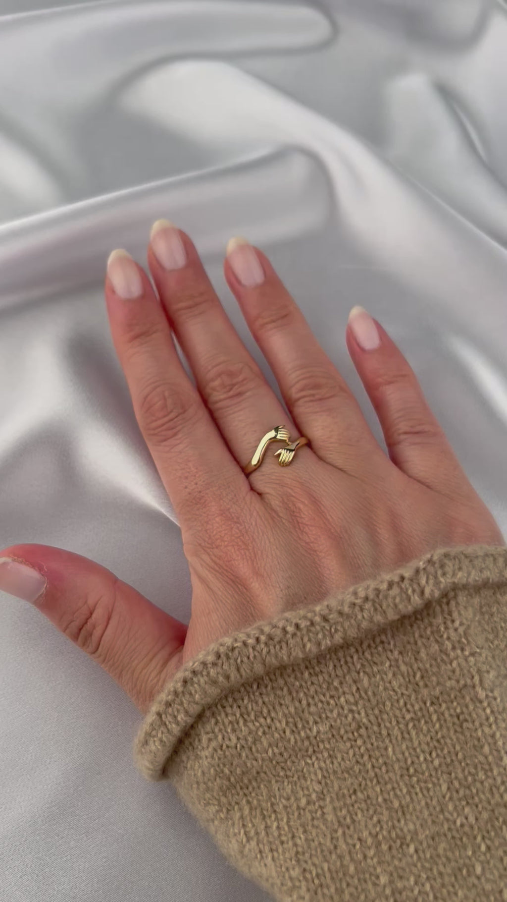 woman with painted nails wearing 14k gold hug ring with long beige sweater on white background show casing the ring
